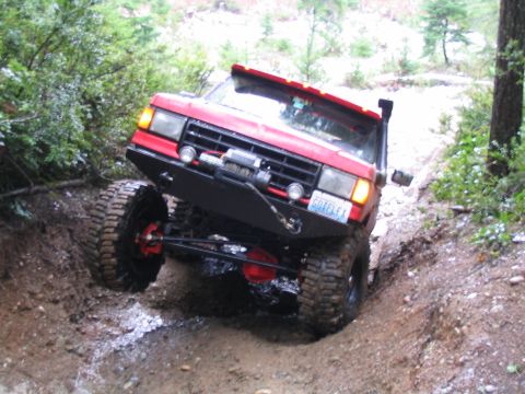 1989 Ford Bronco - A red 1989 Ford Bronco navigates a steep, muddy off-road trail with large tires and a snorkel.