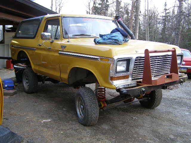 Yellow lifted SUV with a bull bar and snorkel. It has a blue tarp on the hood