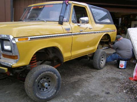 1978 Ford Bronco - A yellow 1978 Ford Bronco is shown with a snorkel and lifted suspension, while a person works underneath it.