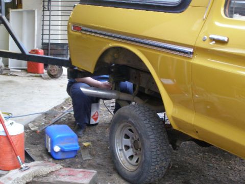 1978 Ford Bronco - Working on the exhaust system of a yellow 1978 Ford Bronco in a garage setting.