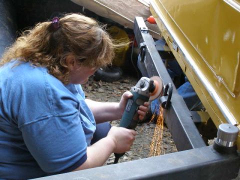 1978 Ford Bronco - A person uses an angle grinder to work on a vehicle's metal frame, creating sparks.