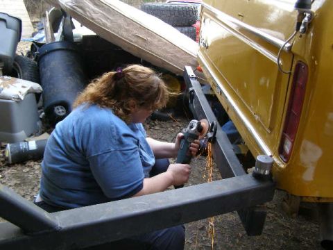 1978 Ford Bronco - A woman uses an angle grinder to modify the rear bumper of a yellow 1978 Ford Bronco.