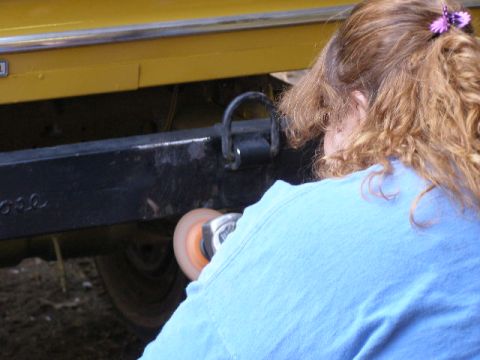 1978 Ford Bronco - A person uses a polishing tool on the bumper of a yellow vehicle.