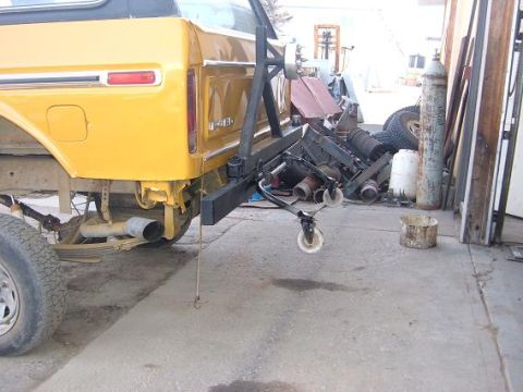 1978 Ford Bronco - The rear of a yellow SUV is shown with its bumper removed, and an engine hoist is attached to the frame.