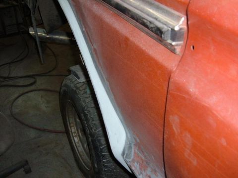 1978 Ford Bronco - Close-up of an orange vehicle's side panel undergoing bodywork, revealing a tire and fender.
