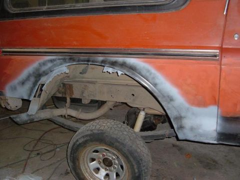 1978 Ford Bronco - This image shows the rear wheel well of an orange SUV, revealing rust damage and areas prepped with primer for repair.
