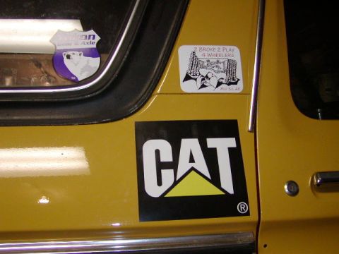 1978 Ford Bronco - A yellow vehicle's side panel displays a large CAT logo and a sticker indicating '2 Broke 2 Play 4 Wheelers'.