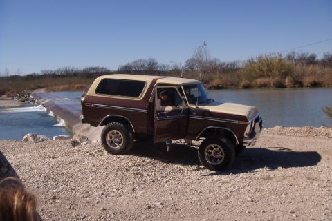 1979 Ford Bronco - A two-tone Ford Bronco is positioned on a dirt path beside a concrete spillway with water flowing over it.