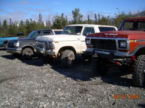1978 Ford Bronco - Several trucks, including a white 1978 Ford Bronco, are parked in a gravel lot under a blue sky.