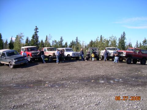 1978 Ford Bronco - Multiple SUVs and trucks are parked in a gravel lot under a clear blue sky.