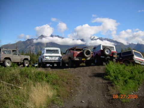 1978 Ford Bronco - A group of SUVs are parked on a dirt road with a scenic mountain backdrop under a cloudy sky.