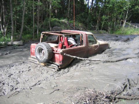 1978 Ford Bronco - A red off-road vehicle is deeply stuck in thick mud, with only its upper body and spare tire visible above the mire.