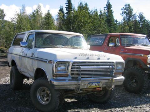 1978 Ford Bronco - A white 1978 Ford Bronco is parked next to a red truck, both modified for off-roading.