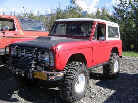 1978 Ford Bronco - A red 1978 Ford Bronco with oversized tires and a black hood scoop is parked next to another vehicle.