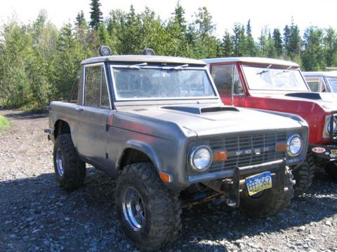 1978 Ford Bronco - This gray Ford Bronco, possibly from the early 1970s, is parked alongside another Bronco in a wooded area.