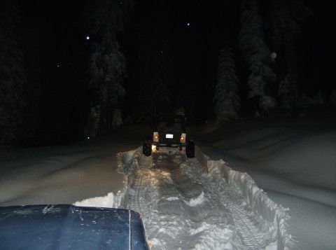 1986 Ford Bronco - Two off-road vehicles navigate a snowy trail under the cover of darkness, with one vehicle following another.