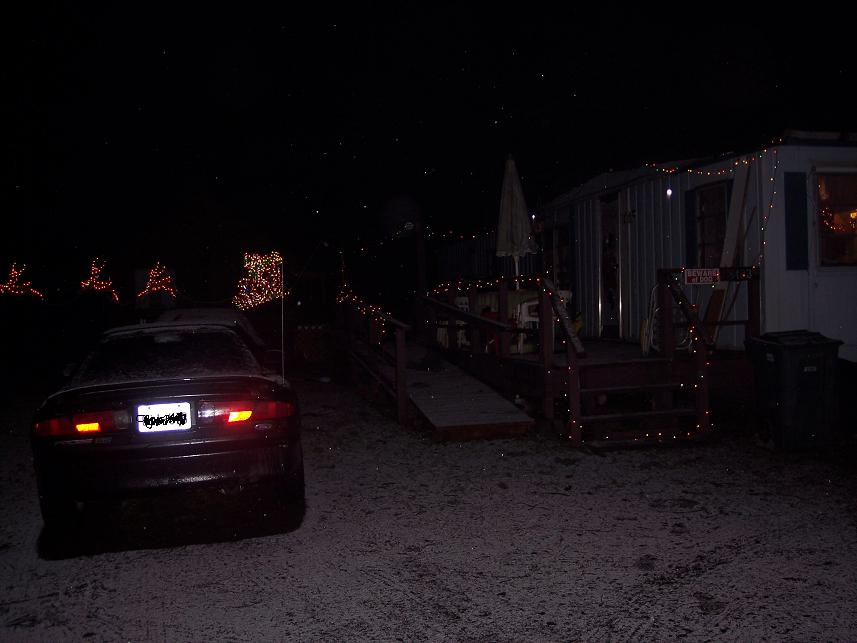 Dark car parked at night beside a trailer strung with Christmas lights