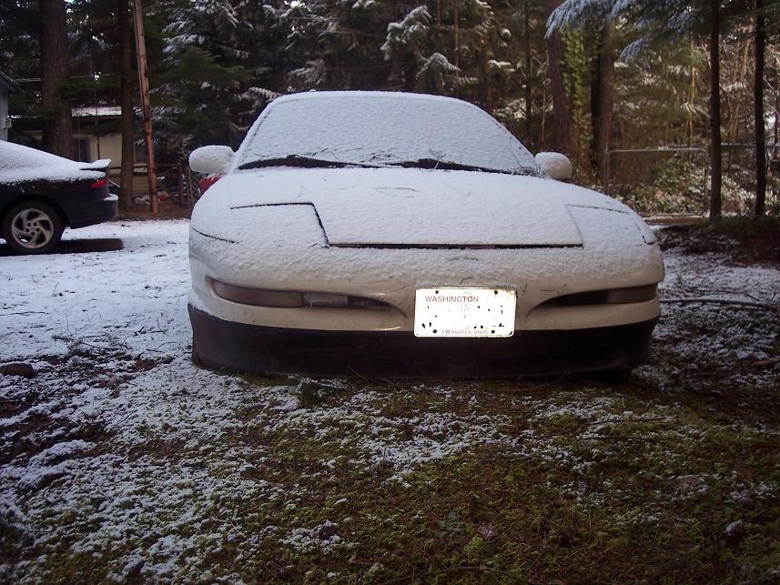 White car with pop-up headlights covered in snow, Washington license plate visible