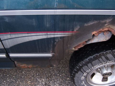 1995 Ford Bronco - The side of a dark green SUV shows significant rust damage, particularly around the rear wheel well and lower body panels.