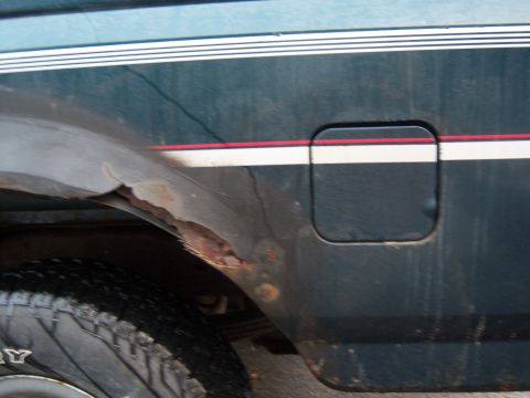 1995 Ford Bronco - The side of a 1995 Ford Bronco displays a fuel door and significant rust around the rear wheel well.