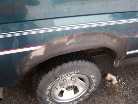 1995 Ford Bronco - Close-up of a rusty wheel well on a green SUV, showing tire and body trim.
