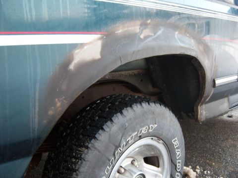 1995 Ford Bronco - Close-up of the rear wheel well on a 1995 Ford Bronco, revealing rust and body damage.