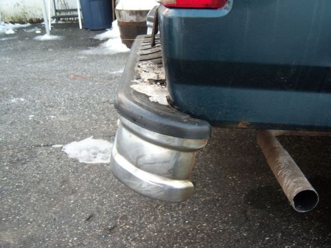 1995 Ford Bronco - Close-up of a vehicle's rear bumper and exhaust pipe, with snow visible on the asphalt.