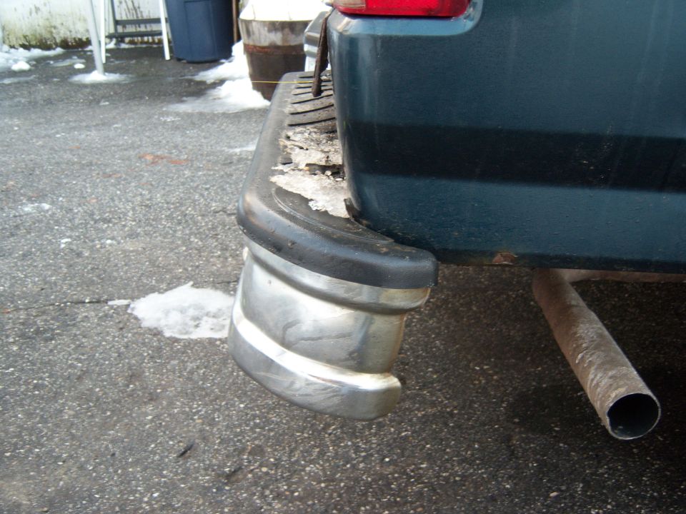 Dark green SUV rear bumper with chrome accents and exhaust pipe, snow on ground