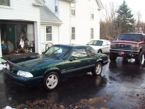 1991 Ford Mustang - A 1991 Ford Mustang coupe is parked in front of a garage, with other vehicles visible.