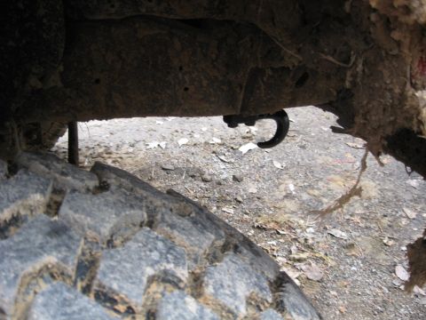 1988 Ford Bronco - Detail of a tow hook mounted on a heavily rusted vehicle frame, with a tire visible.