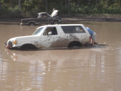1989 Ford Bronco - A white 1989 Ford Bronco is stuck in the mud, with another truck visible in the background.
