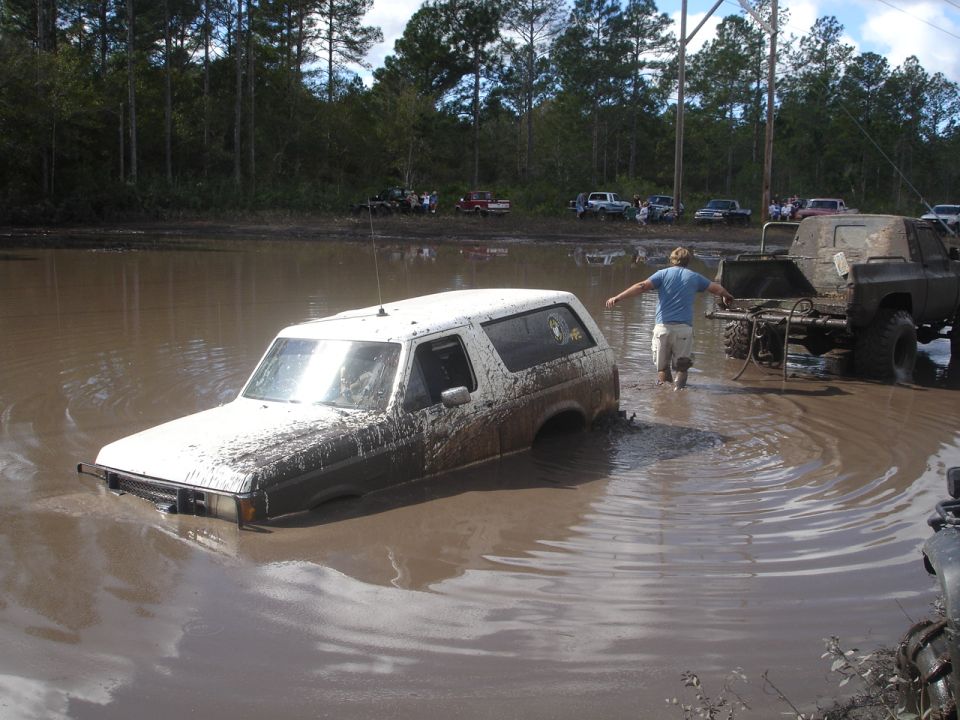 White SUV stuck in mud pit with a man walking nearby