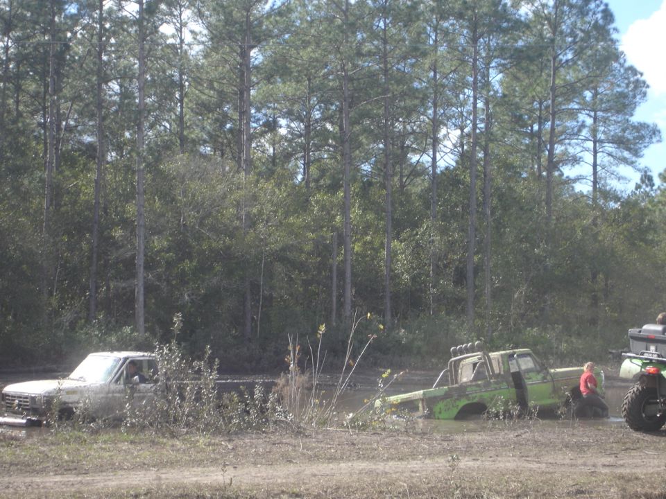 Two trucks stuck in mud with trees in the background