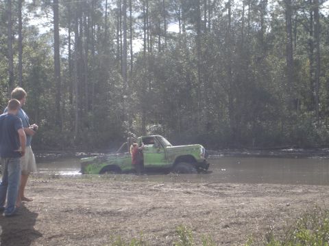 1989 Ford Bronco - A green pickup truck is stuck in the mud with two people watching from the bank.