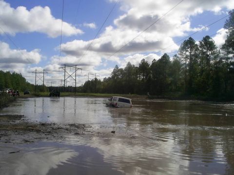 1989 Ford Bronco - A white SUV is stuck in a large puddle of muddy water, with power lines visible in the background.