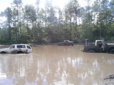 1989 Ford Bronco - Several vehicles are submerged in mud, with people attempting to navigate the difficult terrain.