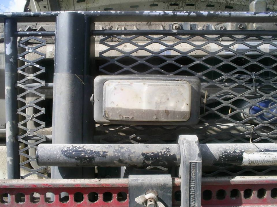 Close-up of a truck's front grille with a diamond pattern mesh and a rectangular auxiliary light. A winch is visible below the grille guard