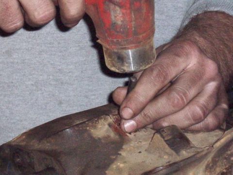 1978 Ford Bronco - Hands are working on a metal part with a hammer and punch tool.