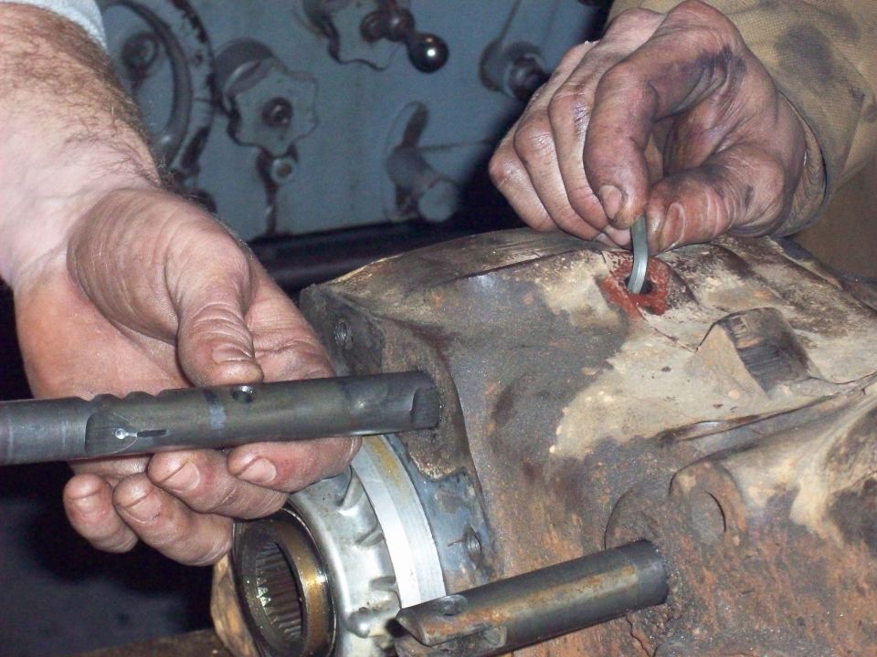 Hands fitting a snap ring and shift rail into a rusty transfer case being rebuilt