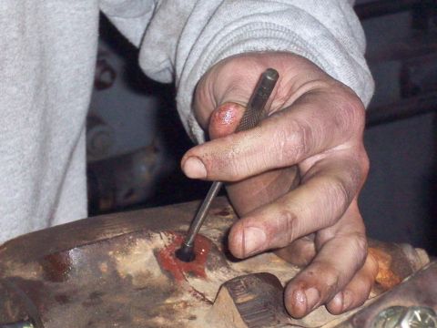 1978 Ford Bronco - A hand works on a rusty metal component, likely part of a vehicle's drivetrain.