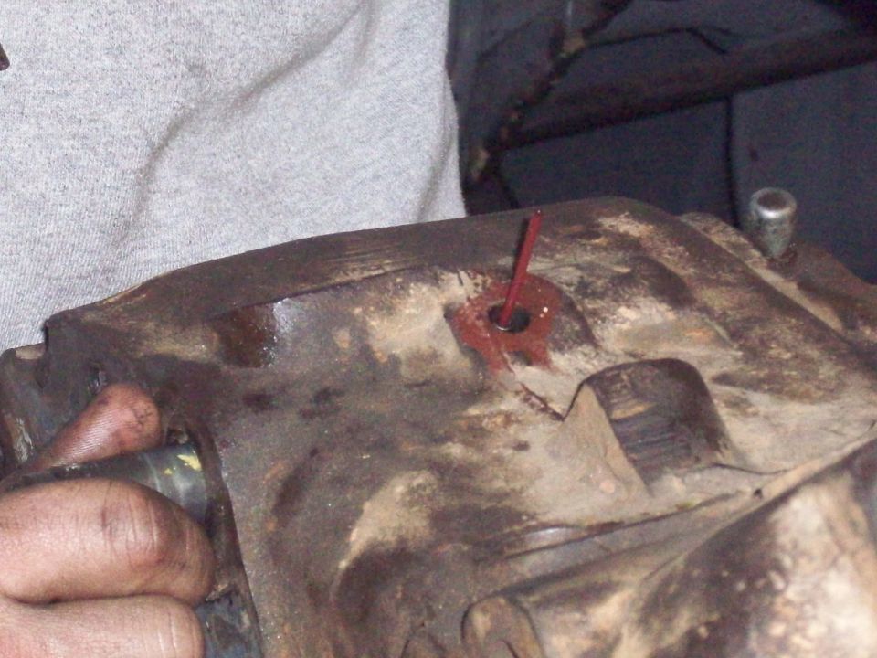 Greasy hand holding a rusty cast-iron gearbox housing with a red-marked pin in its bore