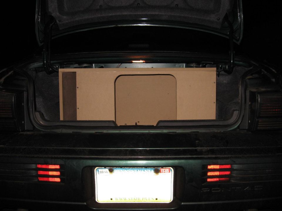 Car trunk open showing a custom-built wooden subwoofer enclosure. License plate is visible