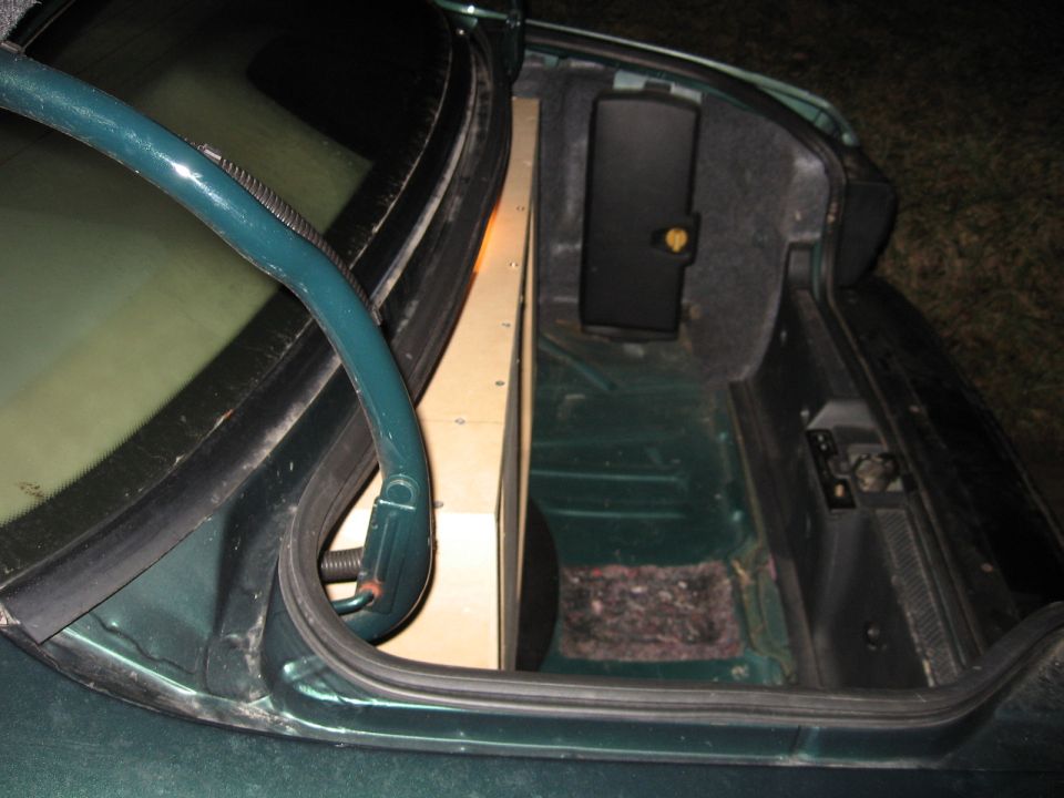 Car trunk with a custom wooden subwoofer box installed. The trunk is dark green