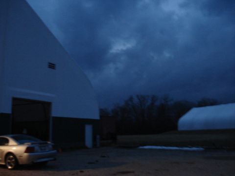 1998 Ford Taurus - A silver coupe, likely a 1999 Ford Mustang, is parked outside a large building as dusk settles under a cloudy sky.