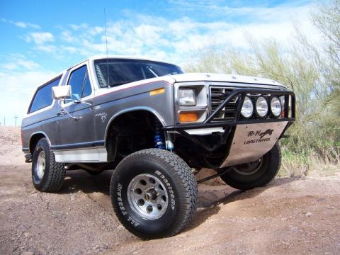 1980 Ford Bronco - Modified 1980 Ford Bronco with off-road tires and suspension sits on a dirt path under a blue sky.