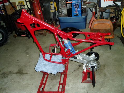 2000 Ford E350 - A red motorcycle frame is shown on a stand, a blue shock absorber and a rear sprocket, suggesting it is undergoing restoration or repair.