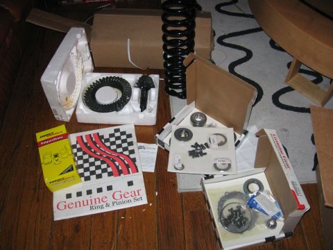 1989 Ford Bronco - Various automotive parts are laid out on a wooden floor, including a ring and pinion set and a coil spring.