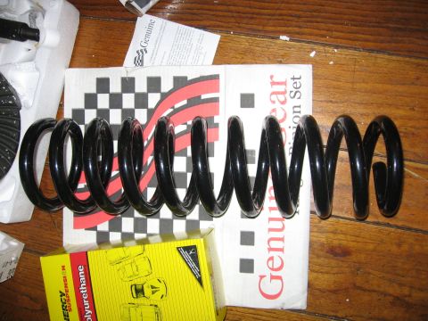 1989 Ford Bronco - New suspension parts laid out on a wooden surface, including a coil spring and packaging.