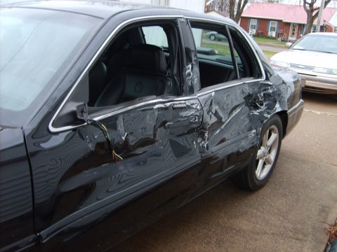 1993 Ford Crown Victoria - This 1993 Ford Crown Victoria shows extensive damage to its driver's side doors, with exposed wiring visible.