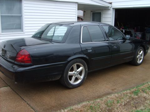 1993 Ford Crown Victoria - This black sedan, likely a 2003 model, is parked outside a garage.